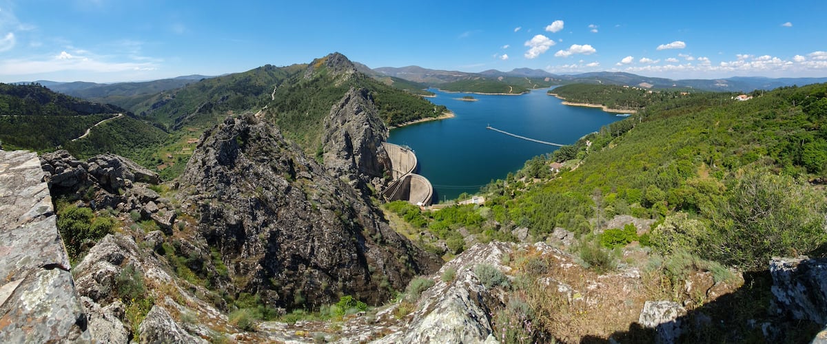 A mountainous landscape with a lake, a dam, and a winding road.