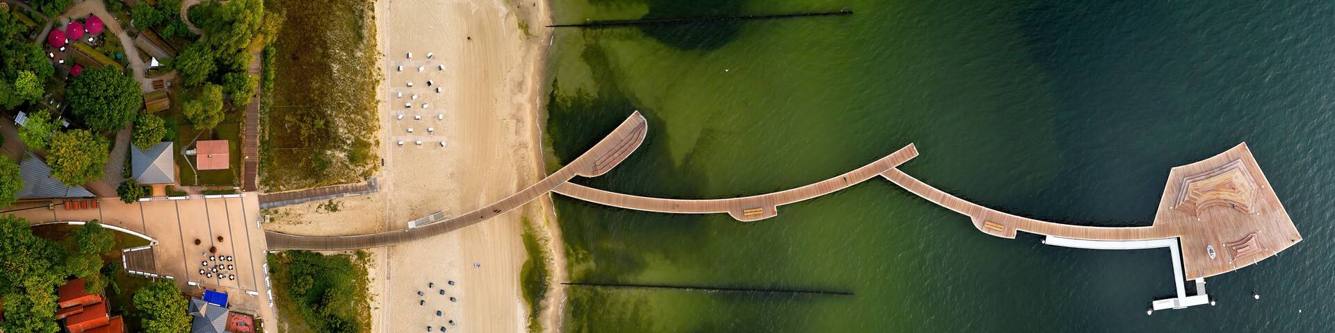 An aerial view of a coastal area with a beach, a wooden pier, and a boat dock.