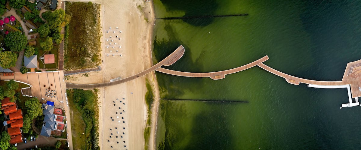 An aerial view of a coastal area with a beach, a wooden pier, and a boat dock.