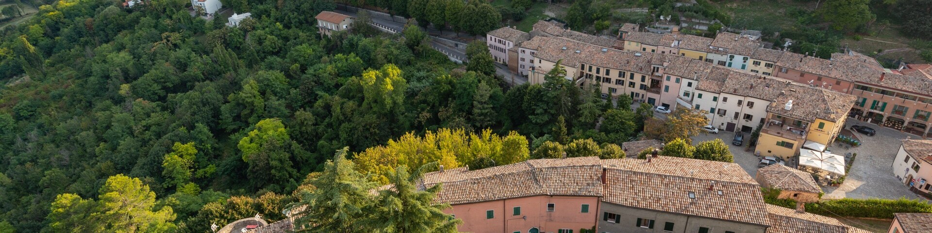 Uma vila numa encosta com edifícios de telhados em terracota, vegetação exuberante e uma estrada sinuosa.