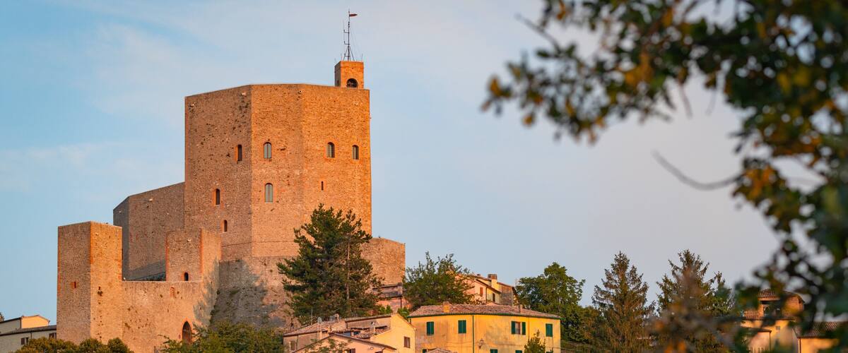 A medieval castle with a prominent tower, surrounded by lush greenery and traditional buildings.