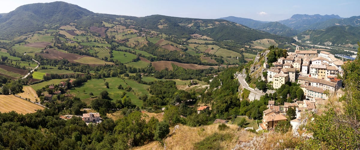 A mountainous landscape with terraced fields, a winding road, and a village with traditional buildings.