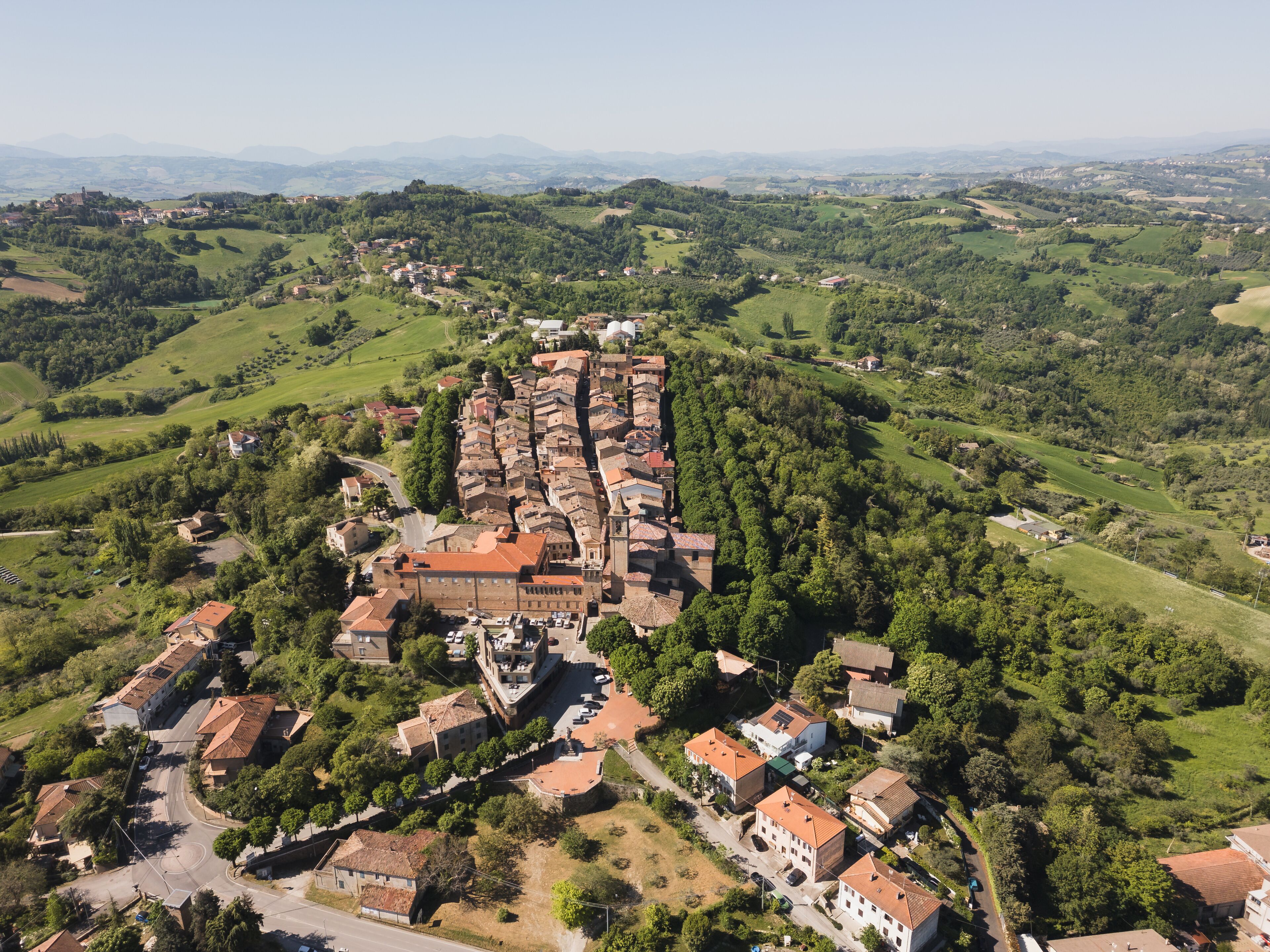 Vista aérea de un pueblo histórico con una iglesia central, rodeado de colinas verdes exuberantes y casas dispersas.
