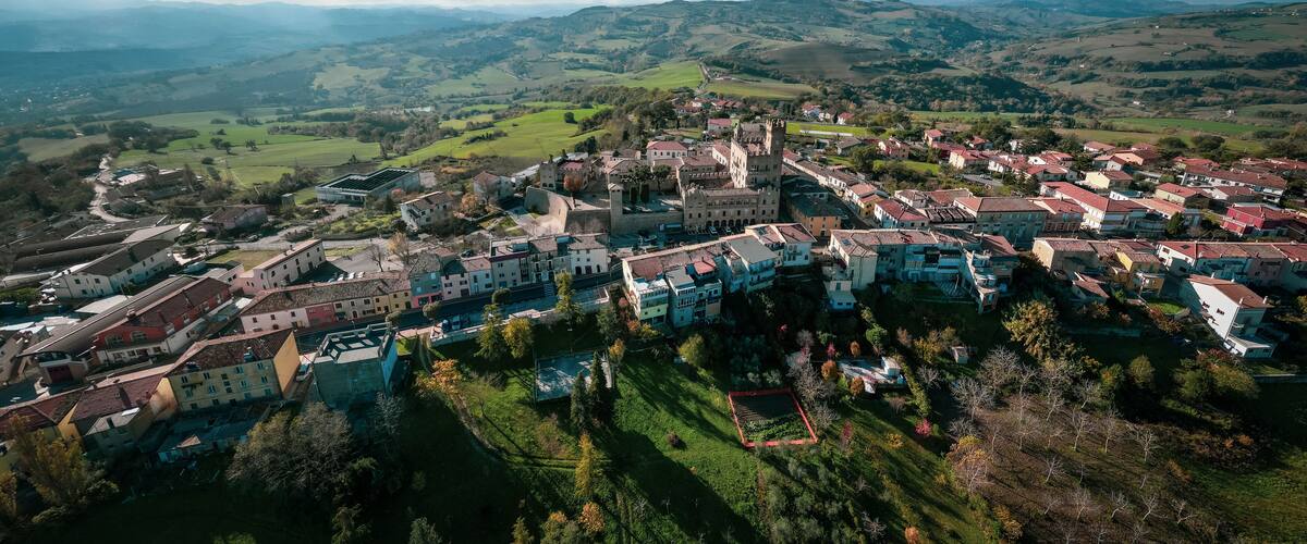 A historic town with medieval architecture, surrounded by rolling hills and green fields.