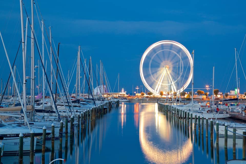 Um porto de iates ao entardecer, com uma grande roda gigante ao fundo.