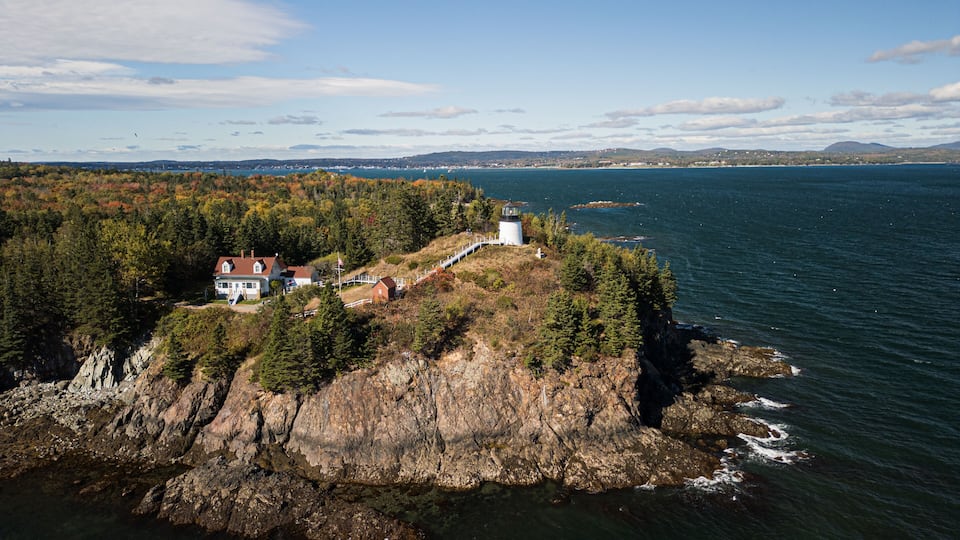A coastal landscape with a lighthouse, a house, and a rocky shoreline.