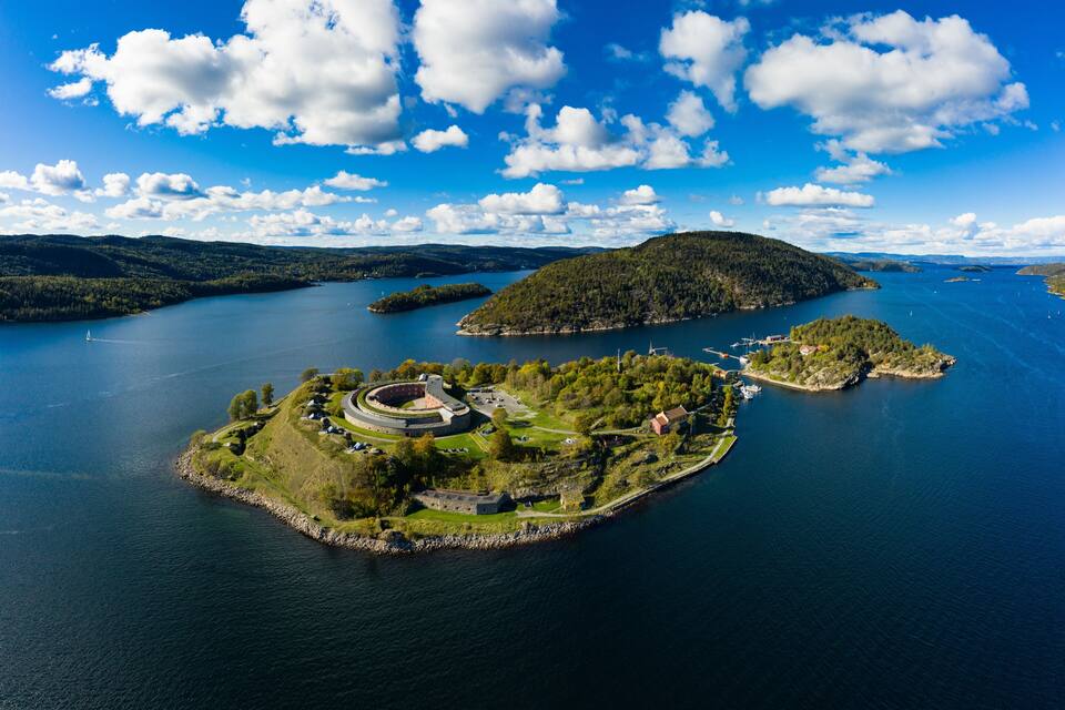 An aerial view of a large lake with several islands, one featuring a circular fortress-like structure surrounded by greenery.