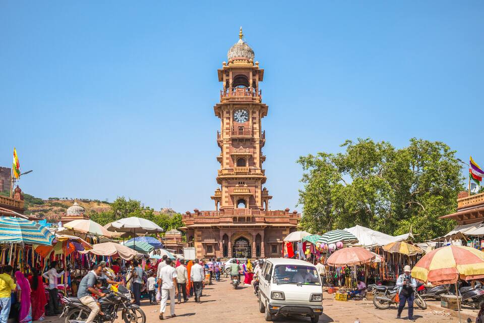 A historic clock tower in a bustling market with various stalls and people.