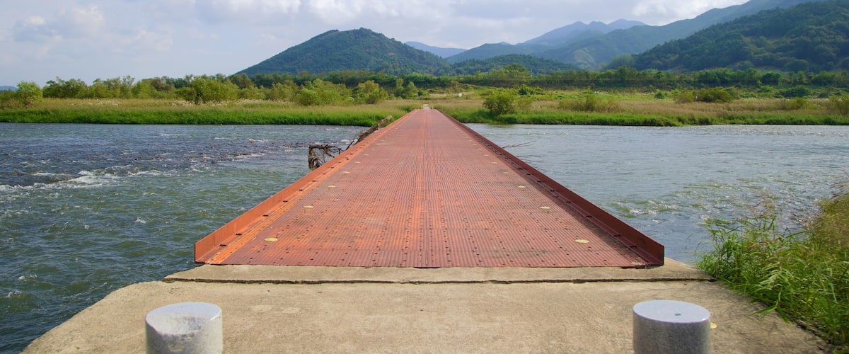 A long, narrow bridge over a river with mountains in the background.