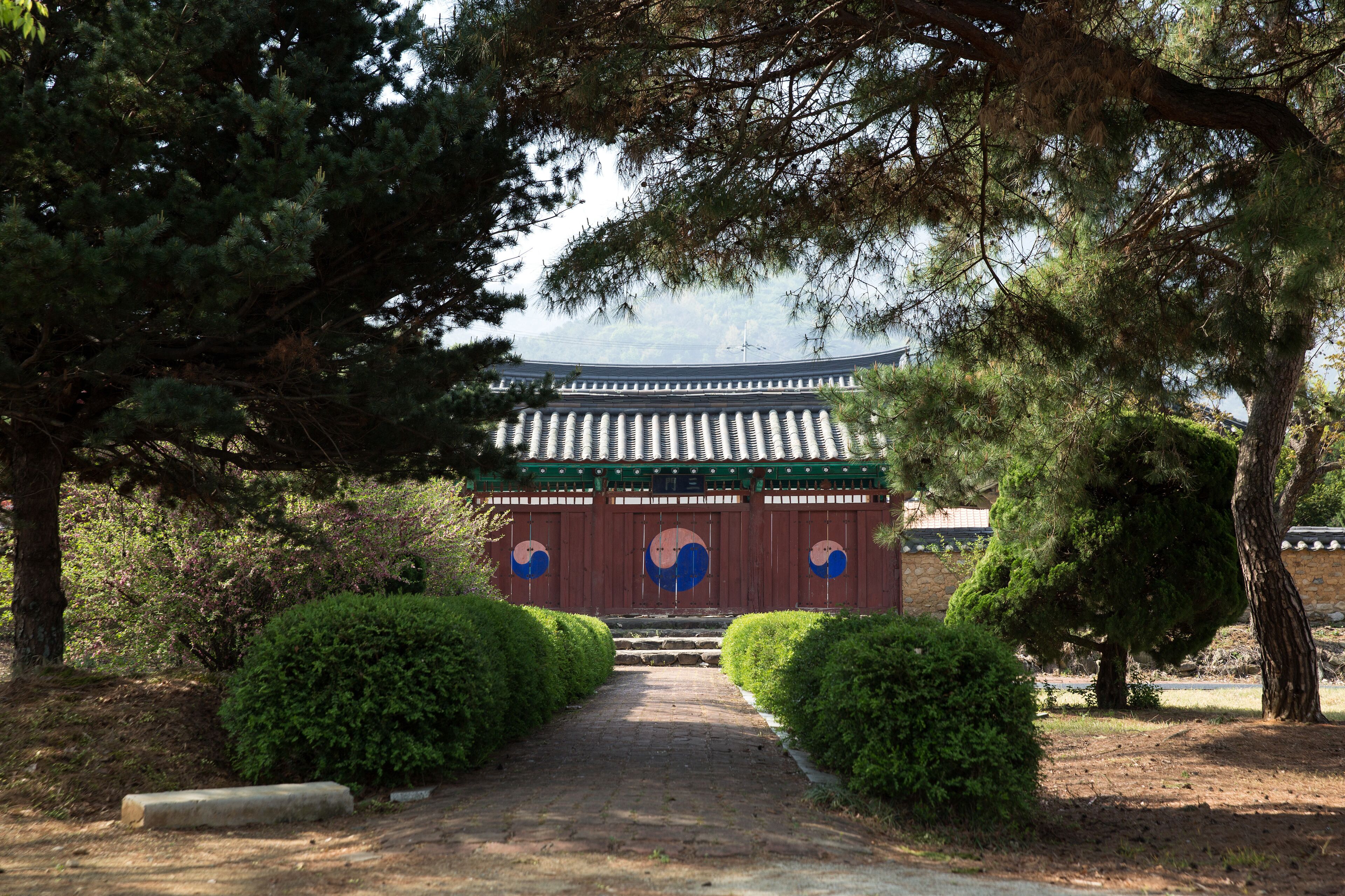 A traditional Korean gate with a tiled roof, surrounded by neatly trimmed bushes and trees.