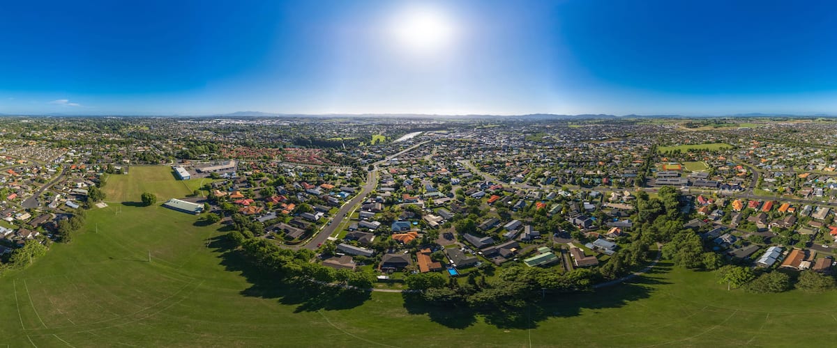 An aerial view of a suburban area with a central road, green spaces, and residential houses.