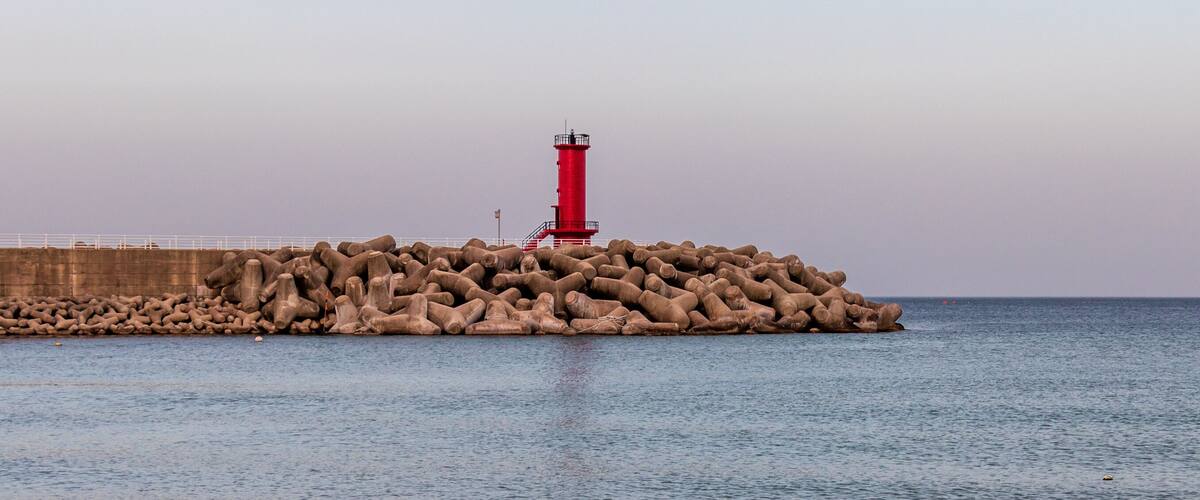 A red lighthouse on a rocky breakwater by the sea.