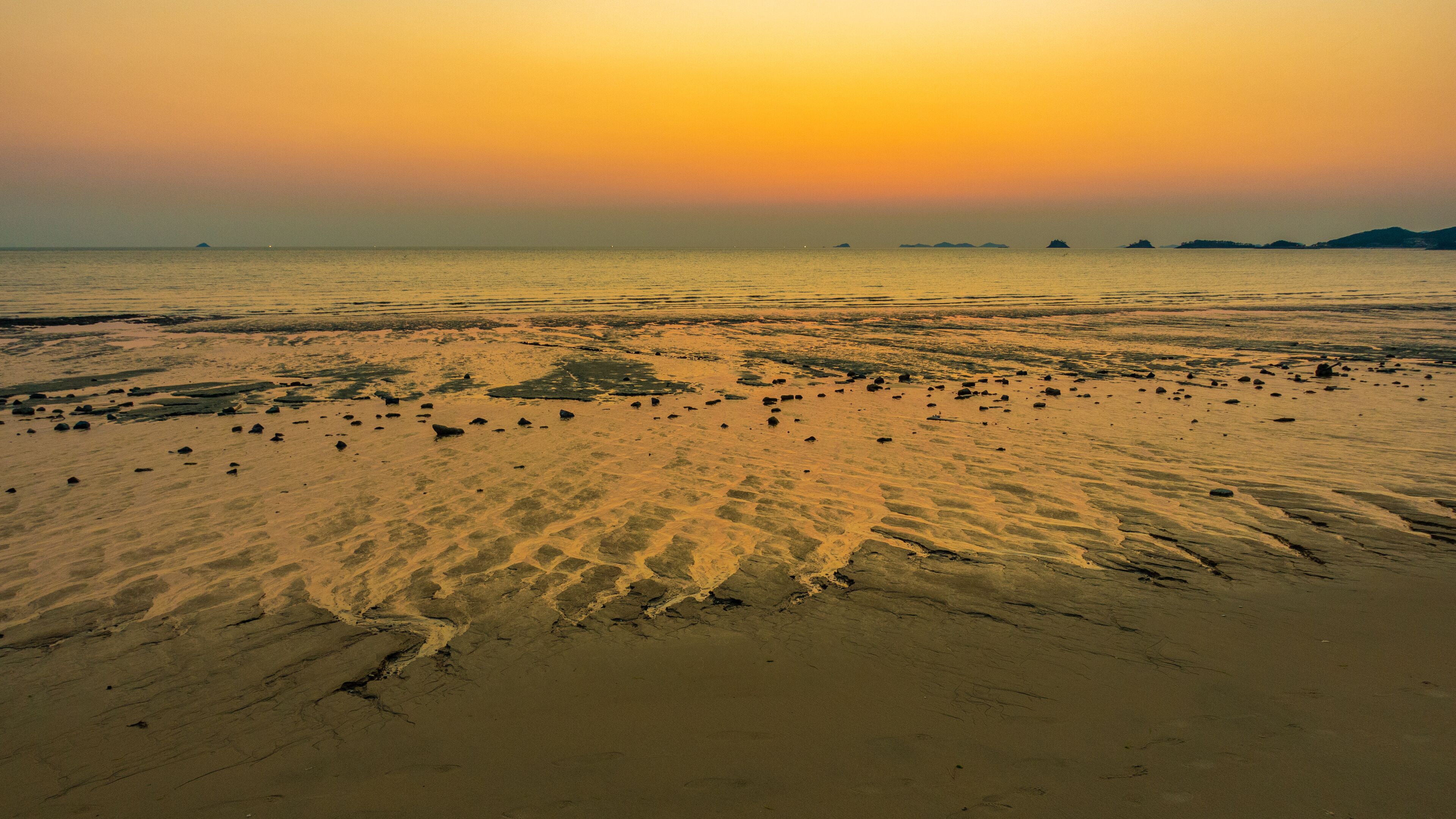 A beach at sunset with sand and scattered rocks.