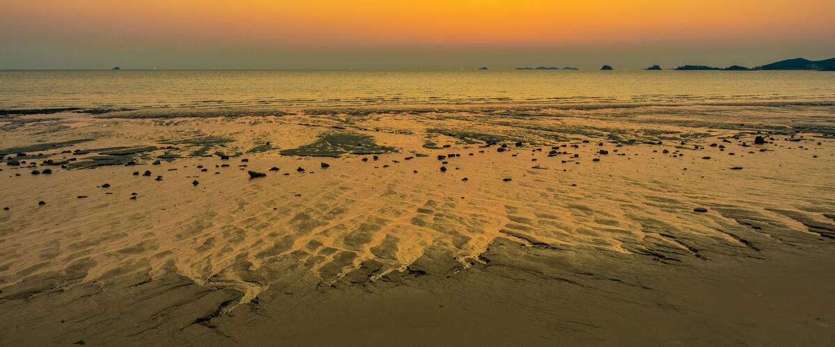 A beach at sunset with sand and scattered rocks.