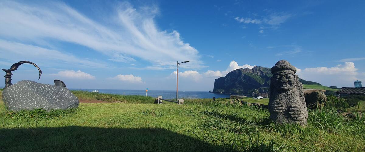 A coastal landscape with a large rock formation, a windmill, and a traditional house.