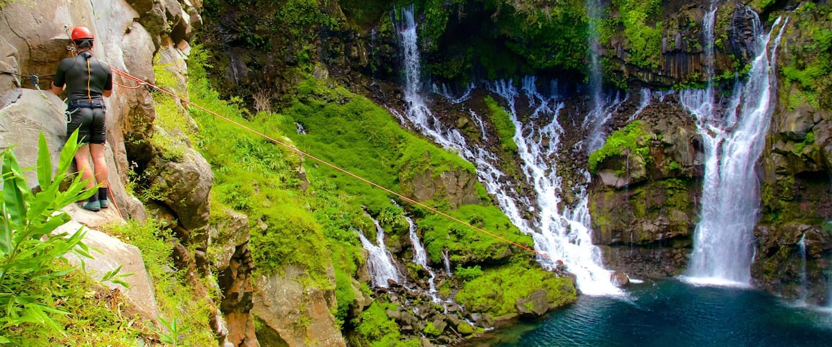 A person rappelling near a multi-tiered waterfall surrounded by lush greenery.