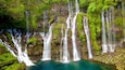 A multi-tiered waterfall cascading into a clear pool surrounded by lush greenery.