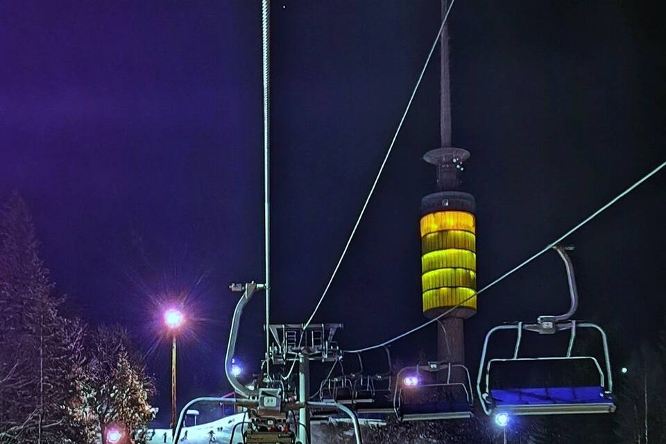 A ski lift at night with illuminated seats and a lit tower.