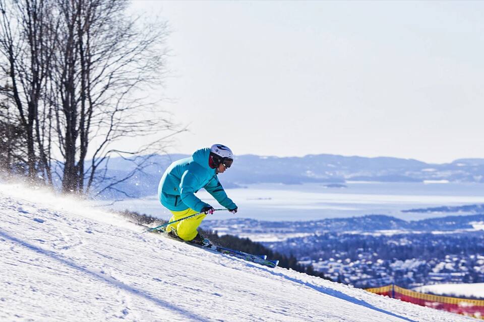 A skier in a blue jacket and yellow pants skiing down a snowy slope with a view of a snow-covered landscape and mountains in the background.