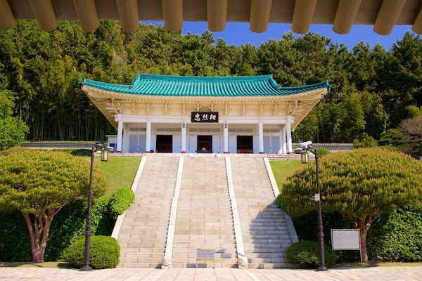 A traditional Korean building with a green roof and white walls, surrounded by lush greenery and a stone staircase leading up to it.