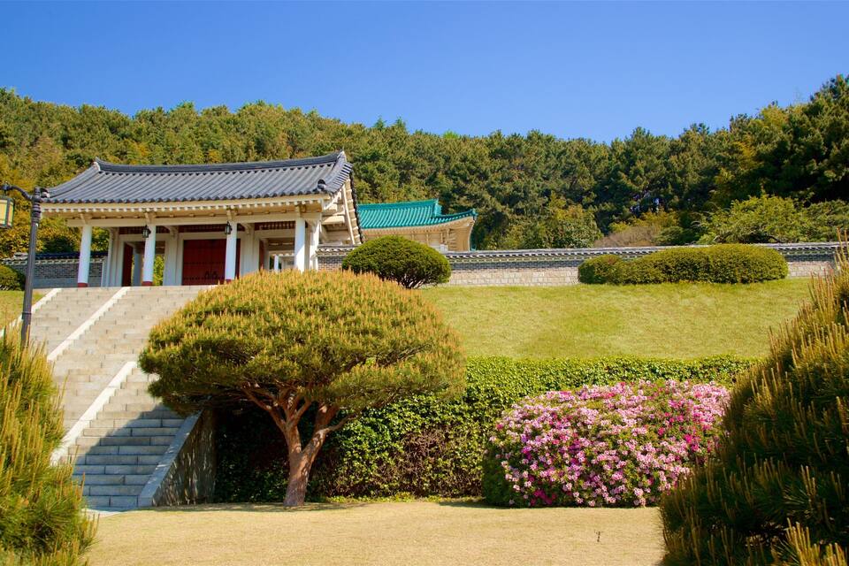 Un edificio coreano tradicional con tejado de baldosas, rodeado de jardines cuidados y una ladera boscosa.