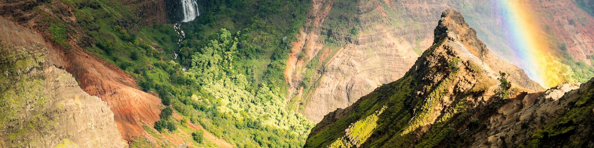 A waterfall cascading down a lush green valley with a visible rainbow.