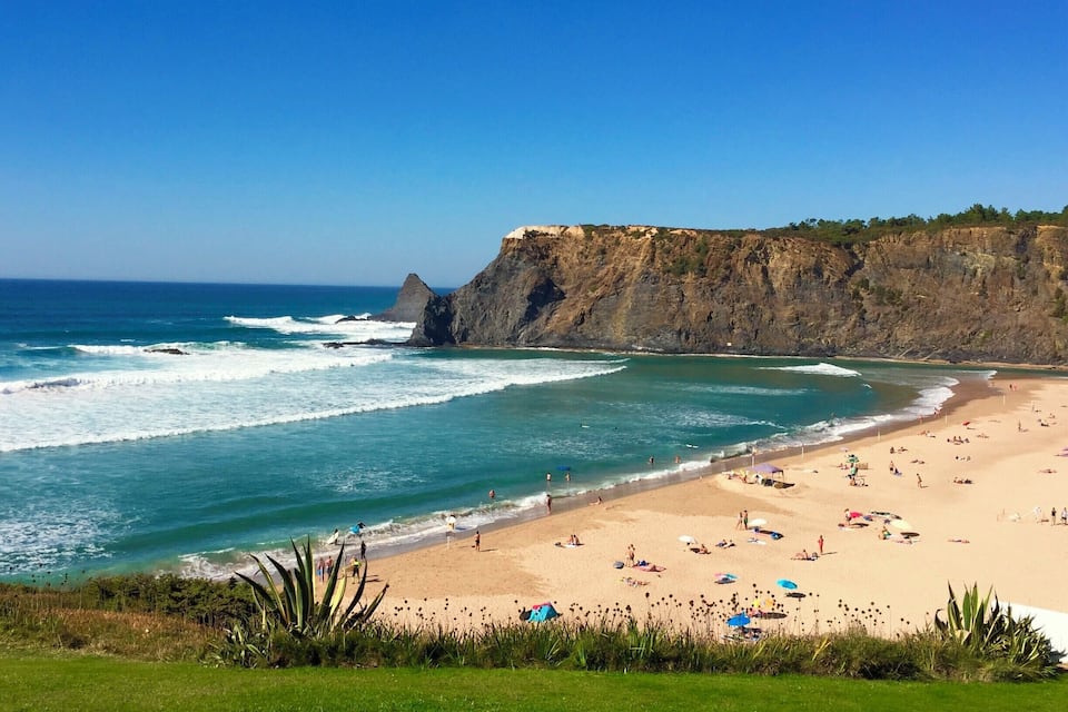 A beach with waves, a rocky cliff, and people sunbathing.