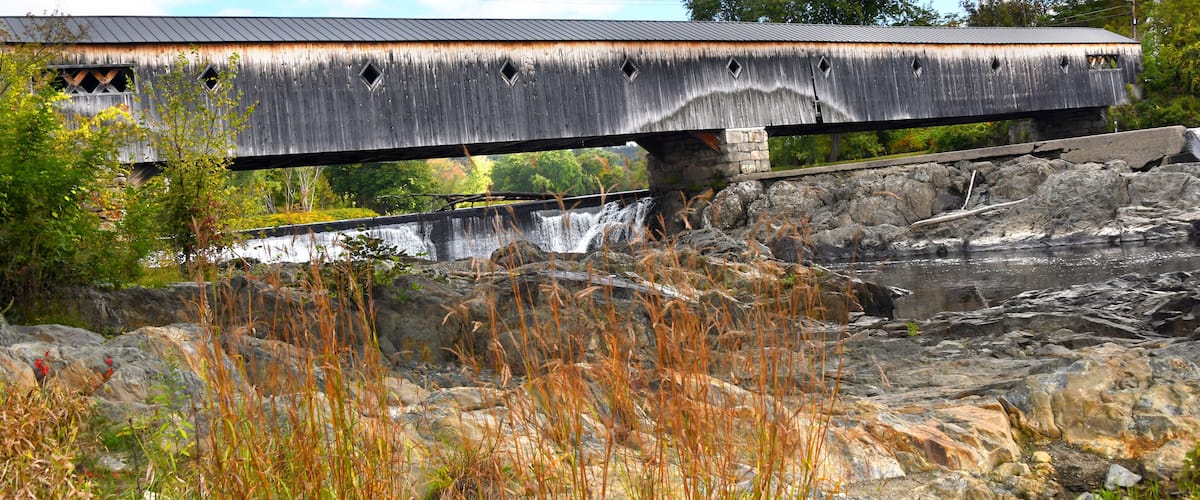 A wooden covered bridge over a rocky river.