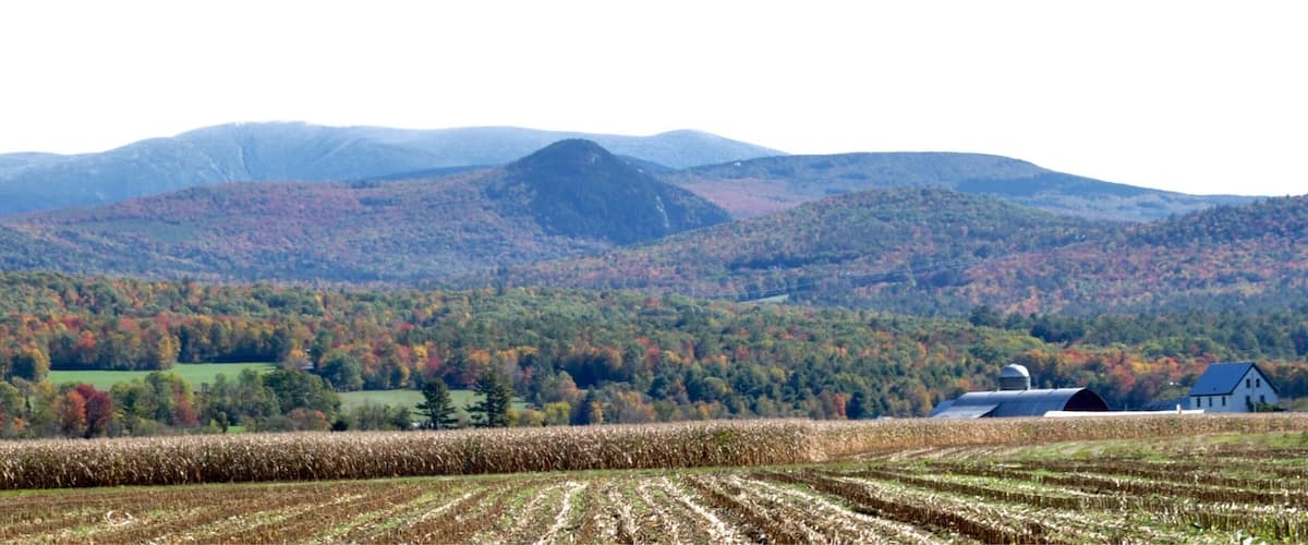 A rural landscape with a field, a barn, and a mountain range.