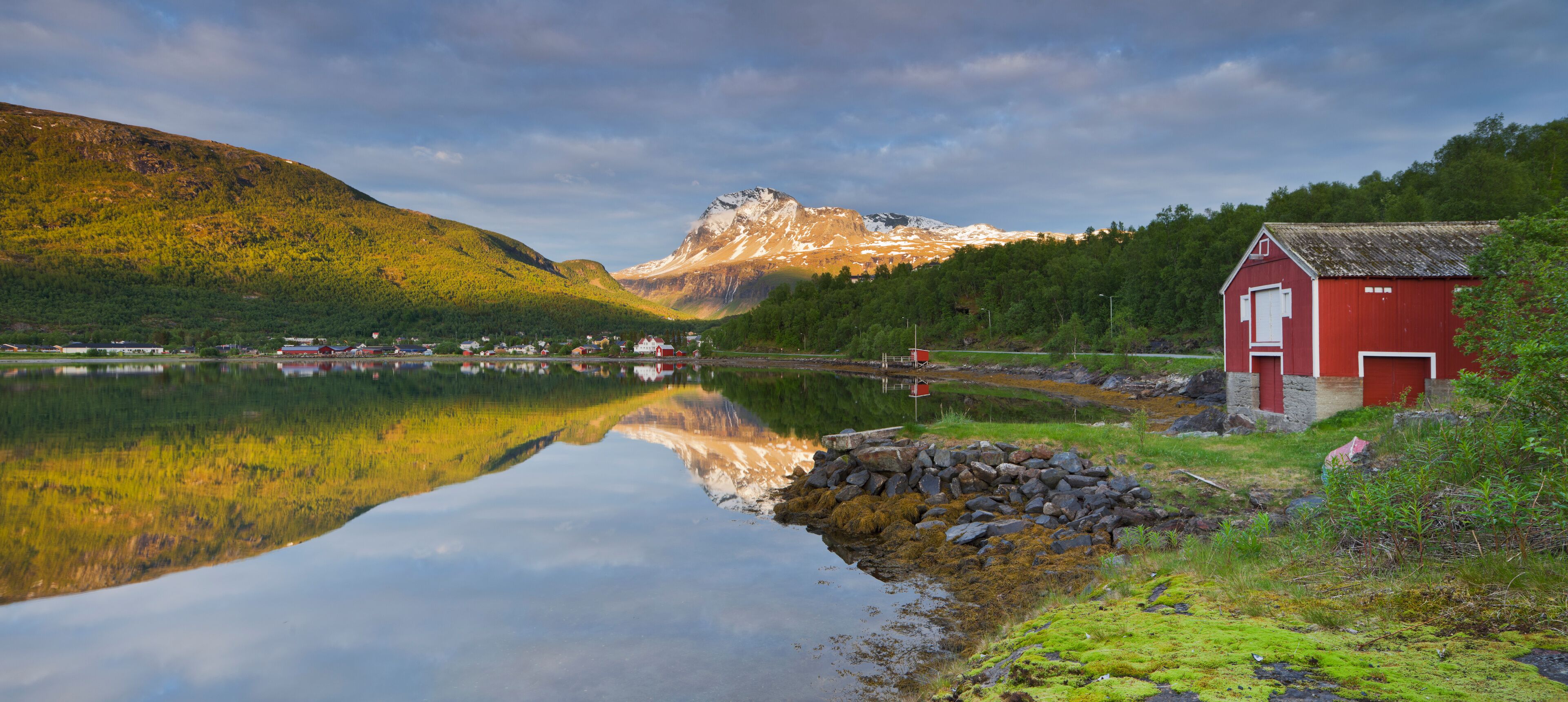 A serene lake with a red building, a mountain in the background, and a clear reflection of the scenery.