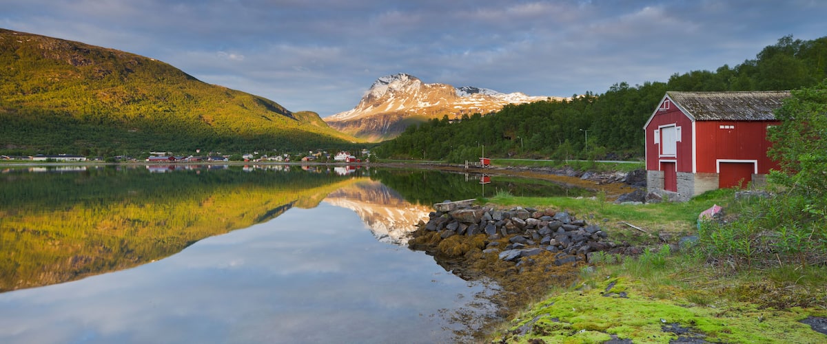 A serene lake with a red building, a mountain in the background, and a clear reflection of the scenery.