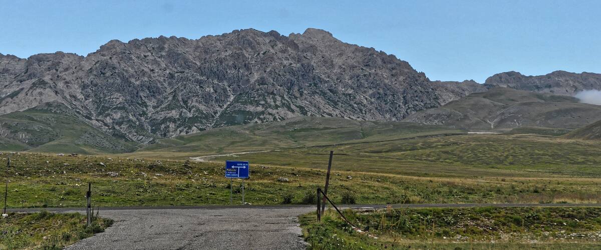 A mountainous landscape with a road leading towards a signpost.