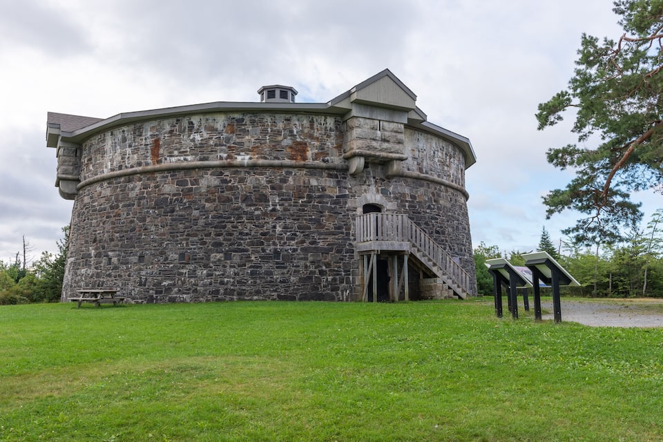 Un edificio in pietra con una torre circolare, una scala in legno e un tavolo da picnic in un'area verde.