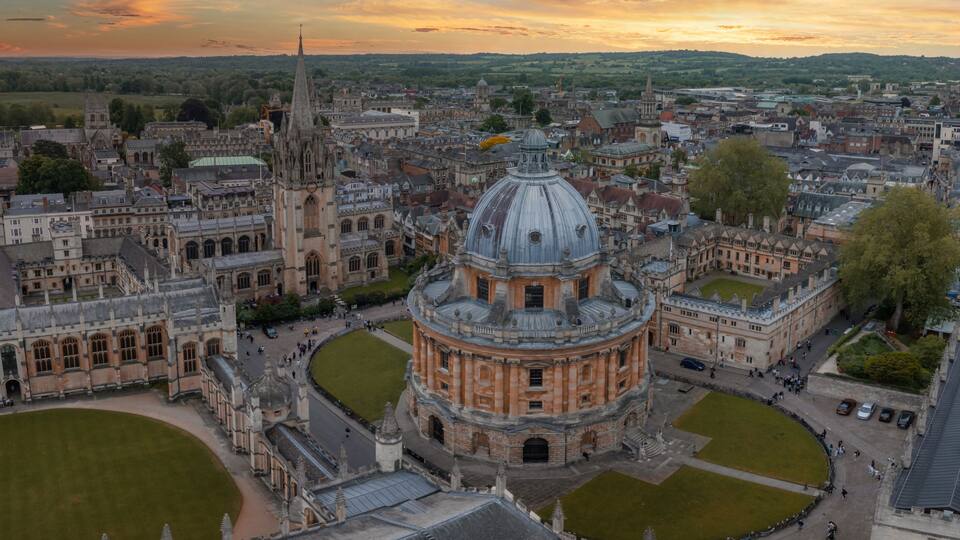 An aerial view of a historic university campus with prominent Gothic architecture, including a large central dome and surrounding quadrangles.
