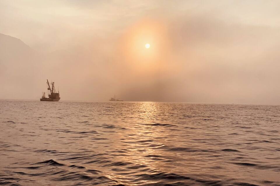 A calm sea with a ship and a distant sun.