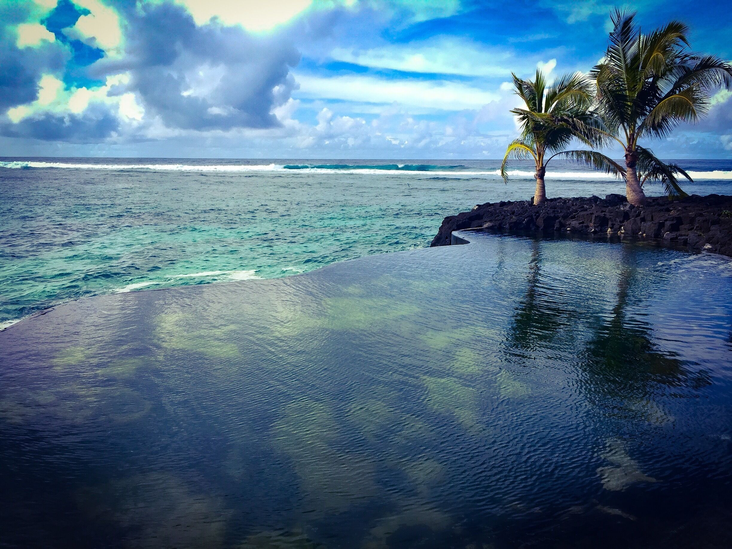 A beach with clear turquoise water, a palm tree, and a rocky outcrop.