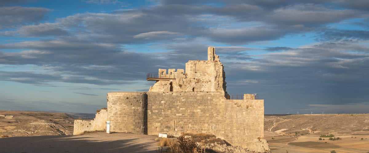 A historic stone fortress with wind turbines in the background.