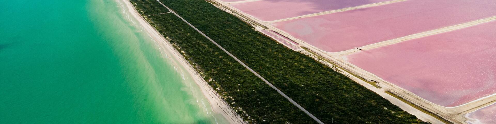 A coastal landscape with a beach, pink salt flats, and turquoise waters.