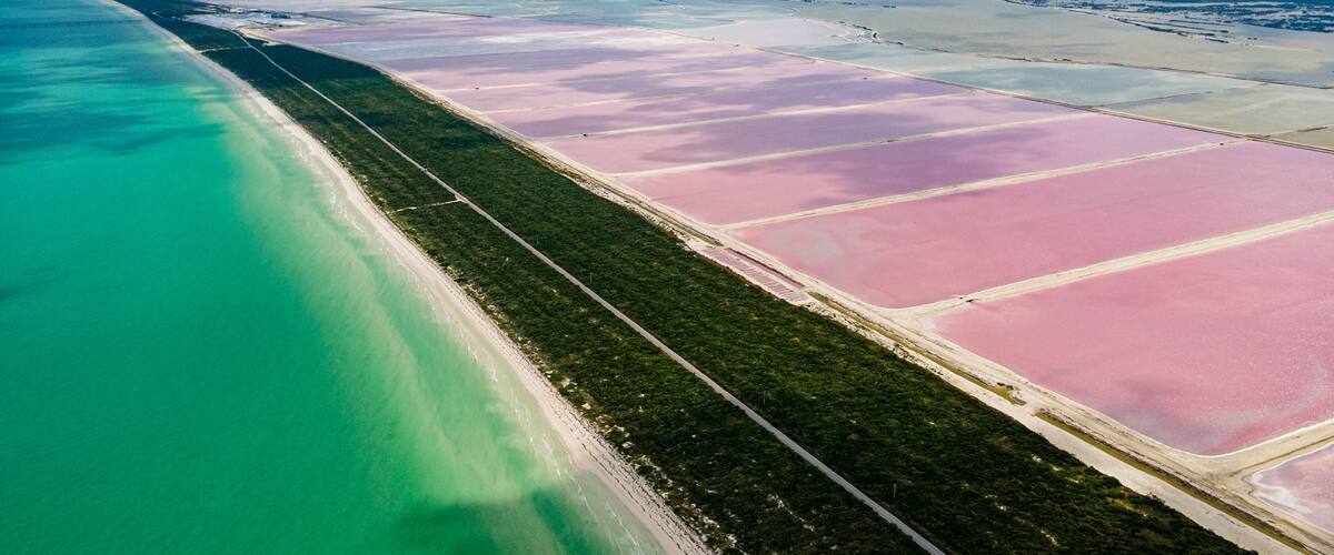 A coastal landscape with a beach, pink salt flats, and turquoise waters.