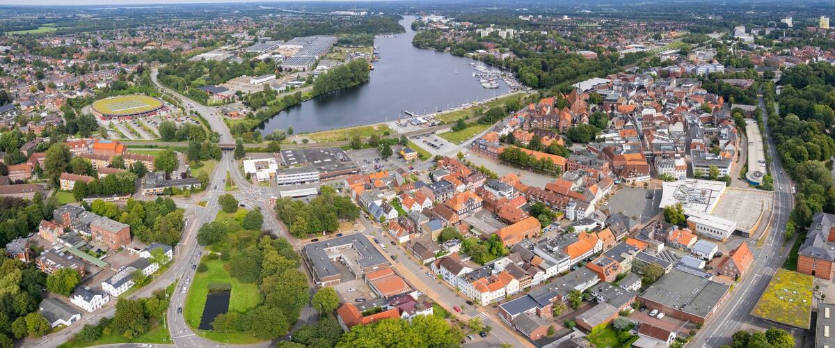An aerial view of a town with a river, green spaces, and a mix of residential and commercial buildings.