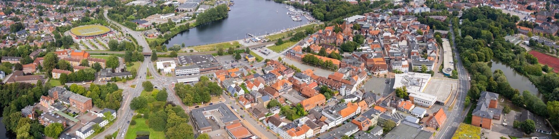 An aerial view of a town with a river, green spaces, and a mix of residential and commercial buildings.