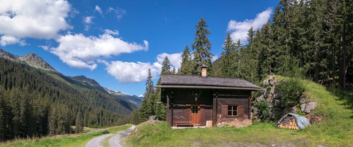 A wooden cabin in a forested valley with mountains in the background.