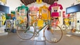 A bicycle in a shop with colorful jerseys hanging in the background.