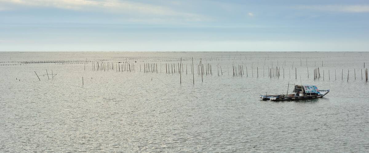 Een rustige zee met een klein bootje en een drijvend afschermingsnet in de verte.