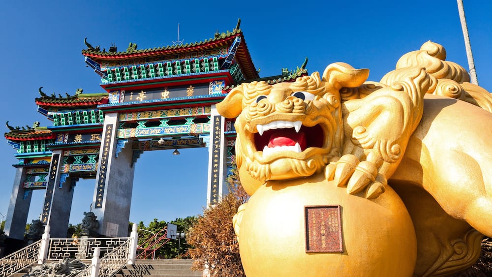 A traditional Chinese gate with ornate decorations and a large golden lion statue in front.