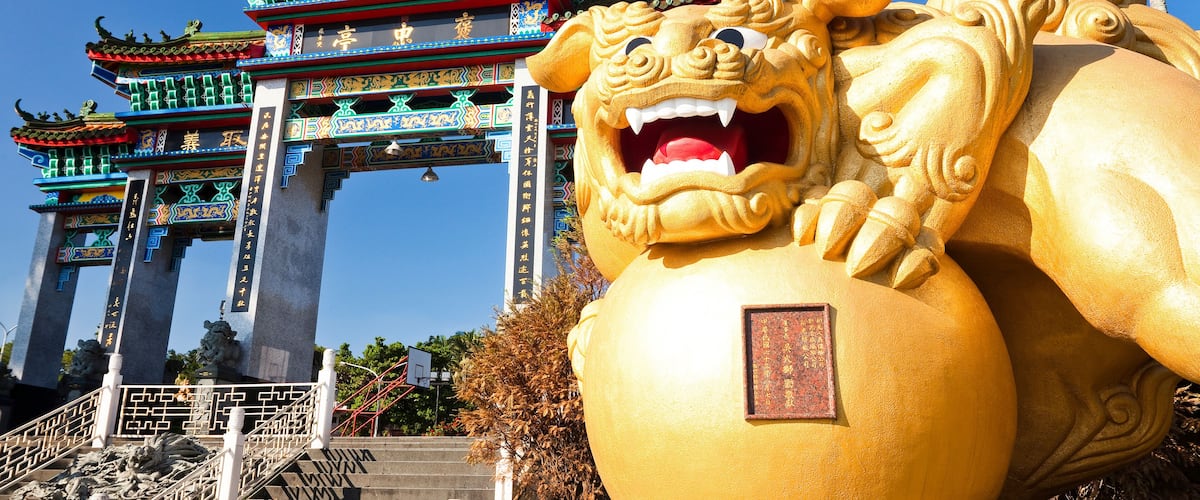 A traditional Chinese gate with ornate decorations and a large golden lion statue in front.