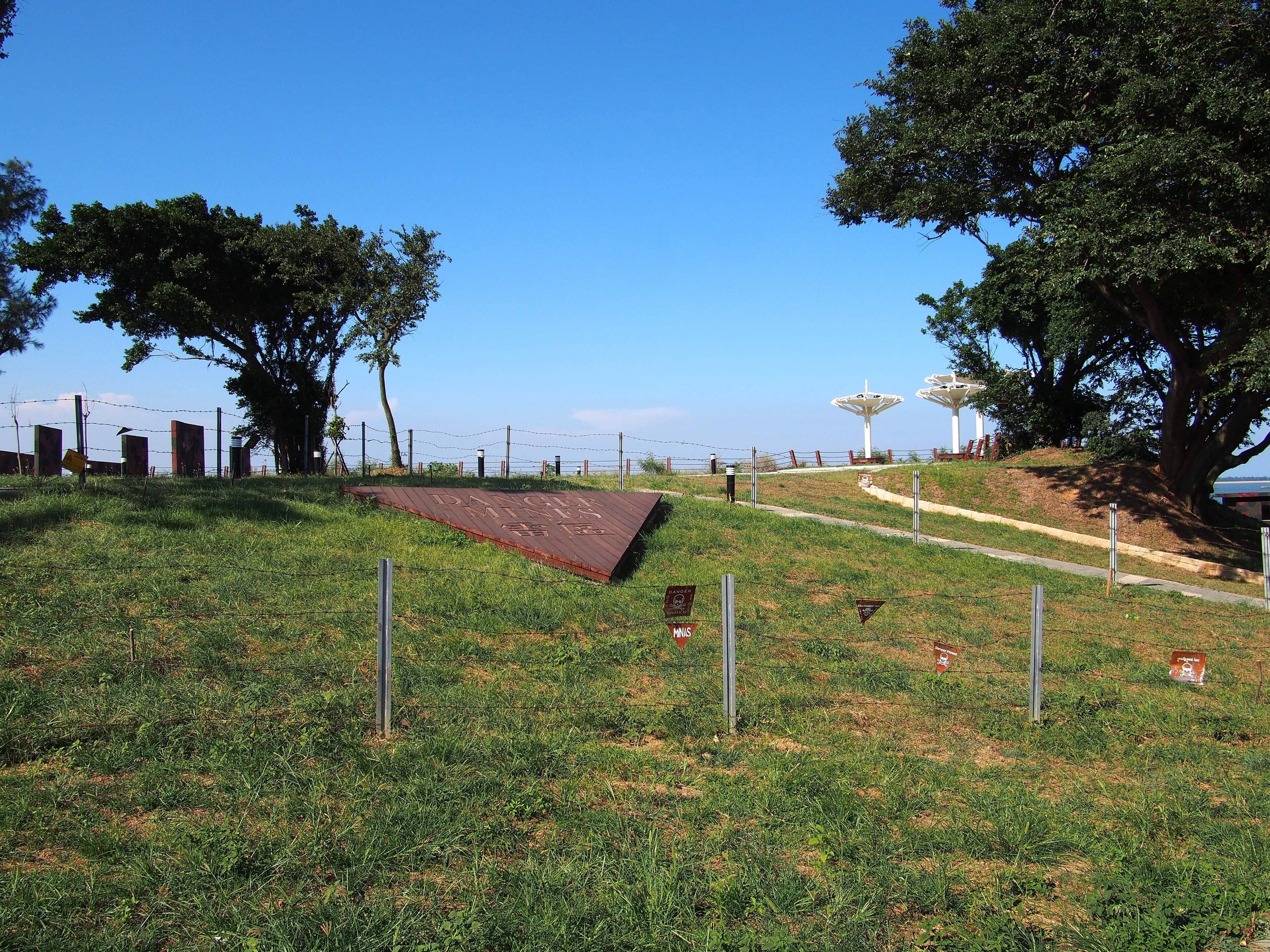A grassy hill with a warning sign, a metal ramp, and a pathway leading to a white structure.