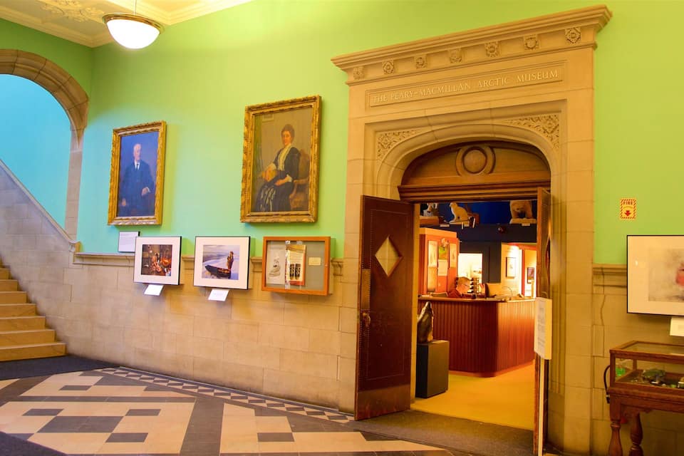 Interior de museo con paredes verdes, retratos enmarcados, una escalera y una chimenea.