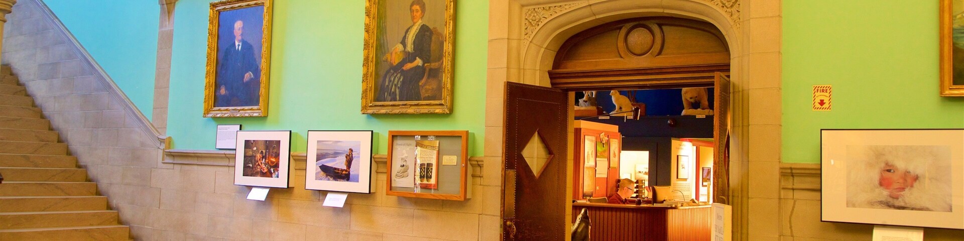 Interior de museo con paredes verdes, retratos enmarcados, una escalera y una chimenea.