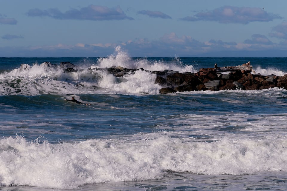 A surfer riding a wave near rocky outcrops in the ocean.